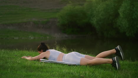 In-the-morning-in-the-Park-a-woman-in-sports-clothes-lying-on-her-stomach-raises-her-arms-and-legs-in-turn.-Exercises-for-a-beautiful-body.-Muscle-stabilizers
